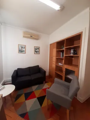 Un box de atención con un sofá, un sillón y un librero de madera empotrado en la pared.