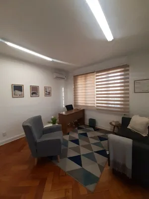 Un box de atención con dos sillones, un escritorio de madera y una ventana a la calle.