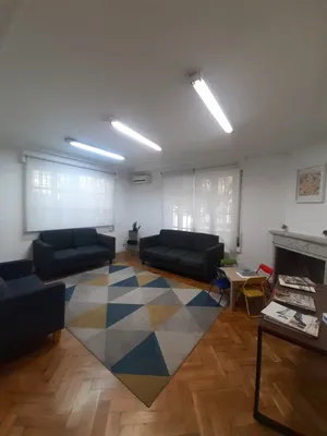 La sala de espera, con dos sofás, una alfombra de colores y ventanales que dan a la calle.