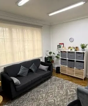 Una sala de atención infantil, con un sofá, una casa de muñecas de madera y estanterías con juegos.